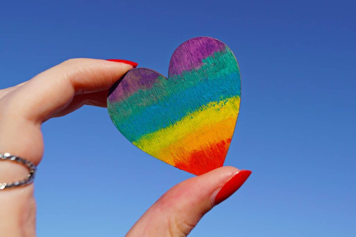 Eine Hand hält ein Herz aus Papier, das in Regenbogenfarben angemalt ist.