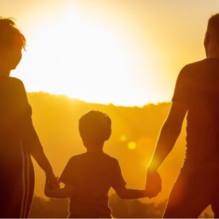 Zwei Eltern und ihr Kind schauen auf den Sonnenuntergang zu