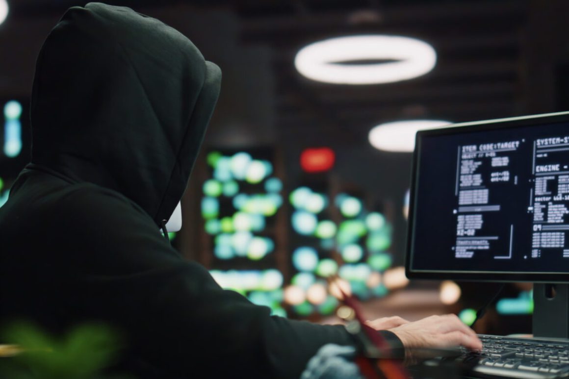 A guy is sitting in front of a monitor. He is wearing a black hoodie, Only his back is shown. The rooom and mood is dark. Radikalisierung, Jugend, online.